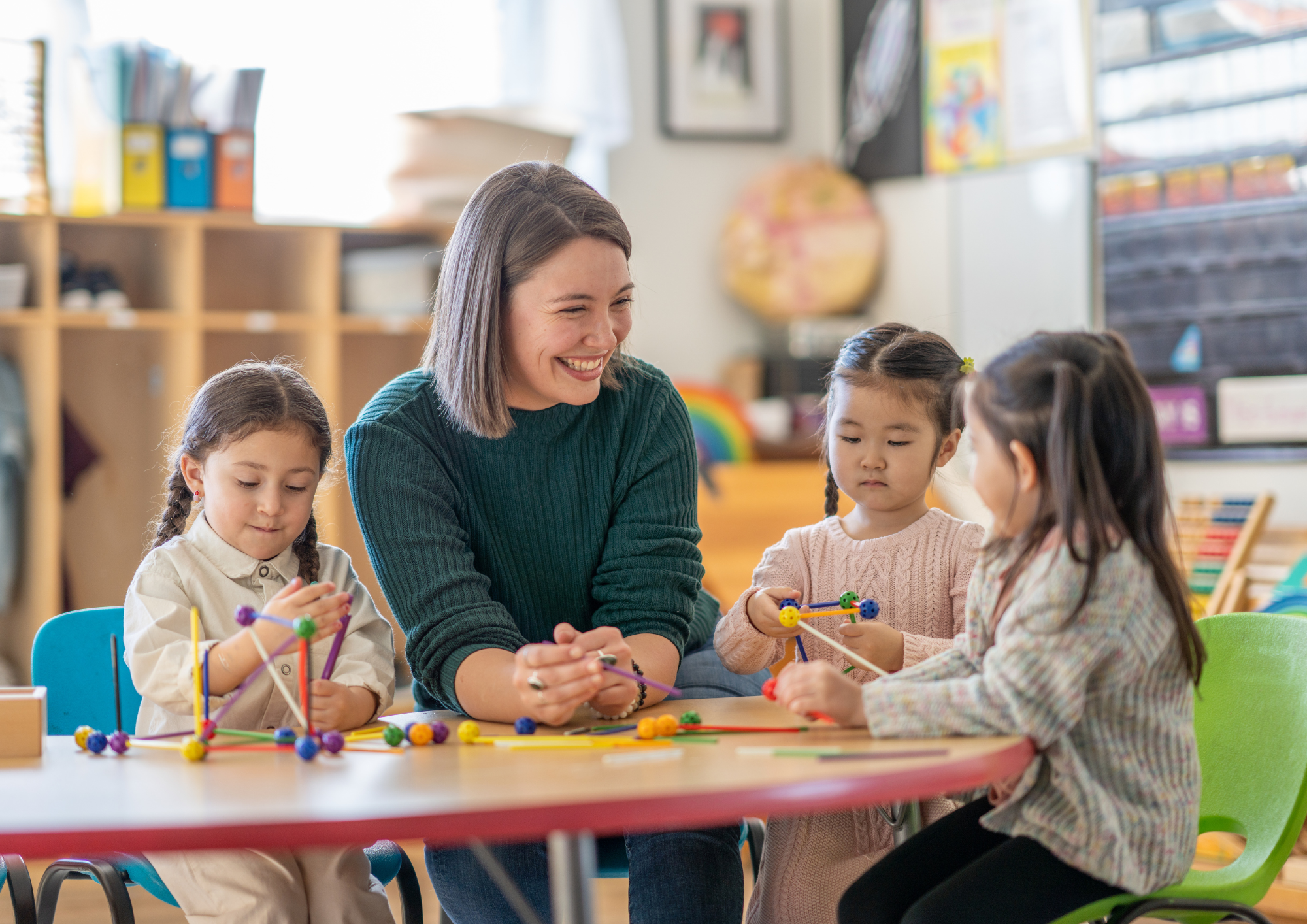 Junge Erzieherin sitzt mit Kindern am Tisch in Kita